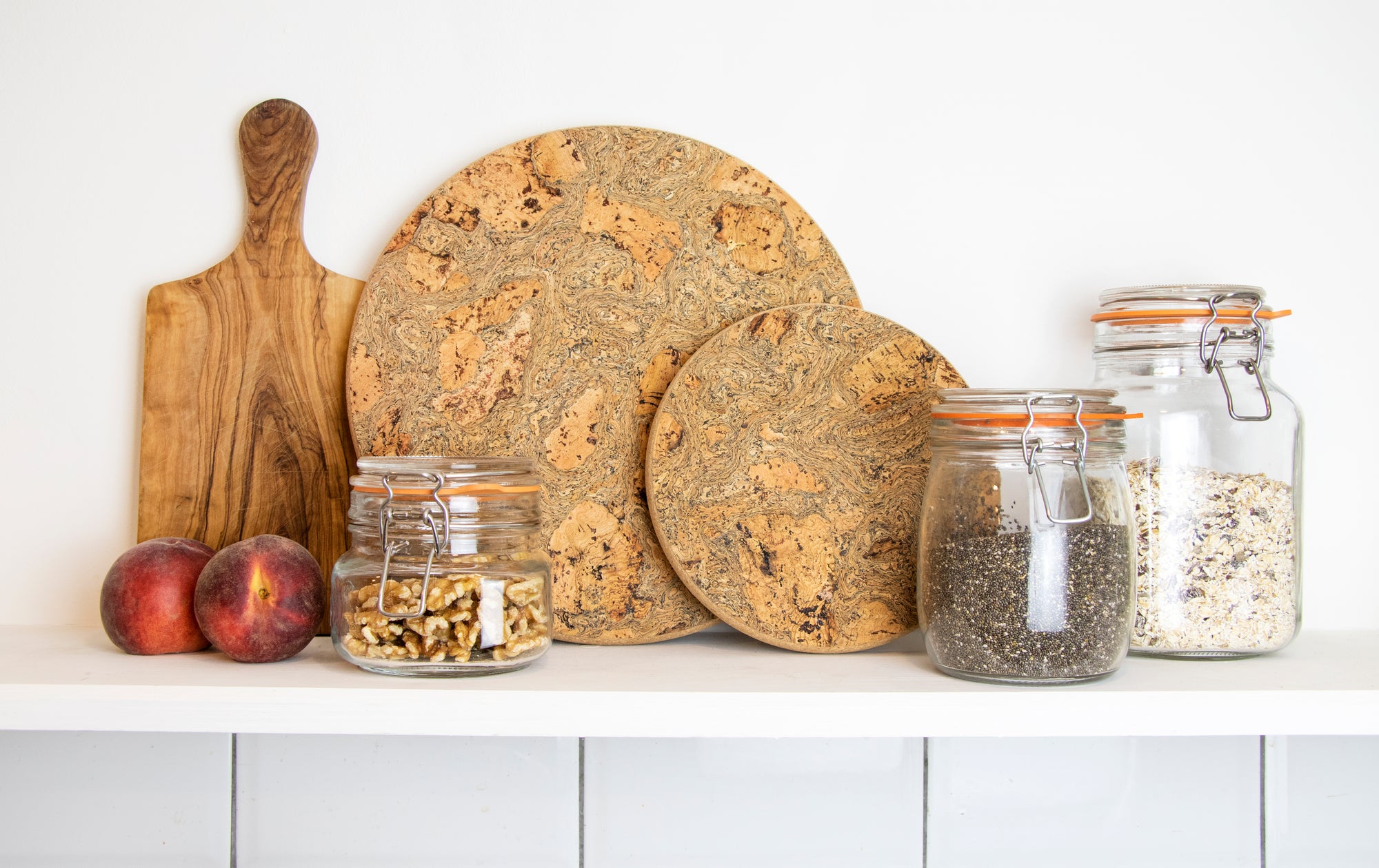 Chunky Cork Trivets in small and medium made with eco friendly cork displayed on a shelf with glass jars and wooden chopping board.